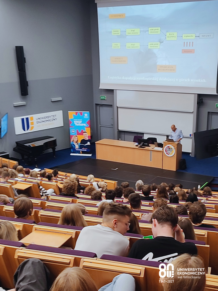 Aula CKU UEW wypełniona blisko czterystoma uczniami. Zdjęcie wykonane zostało z górnej części auli. Na pierwszym planie znajdują się siedzący w ławkach uczniowie. Na drugim planie, w dole, widać prowadzącego dr inż. Pawła Michalskiego.