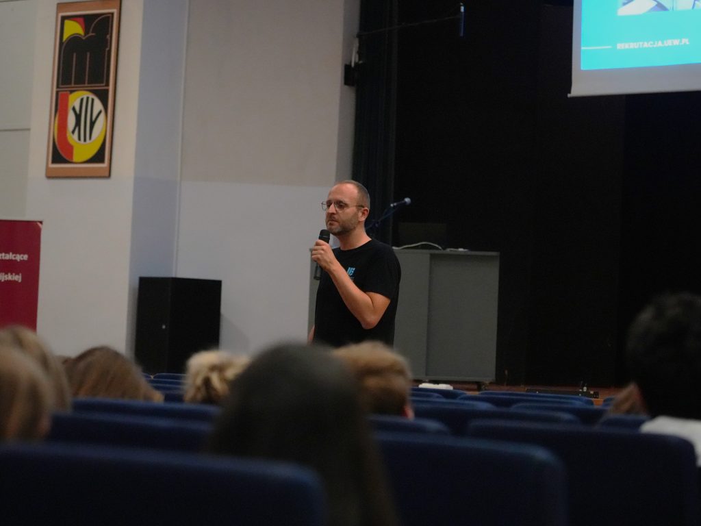Aula XIV Liceum Ogólnokształcącego we Wrocławiu. Krystian Piątek z Sekcji Promocji Kształcenia Uniwersytetu Ekonomicznego we Wrocławiu, prezentuje ofertę edukacyjną uczelni. W sali przed prelegentem znajduje się około 50 uczniów klas maturalnych. 